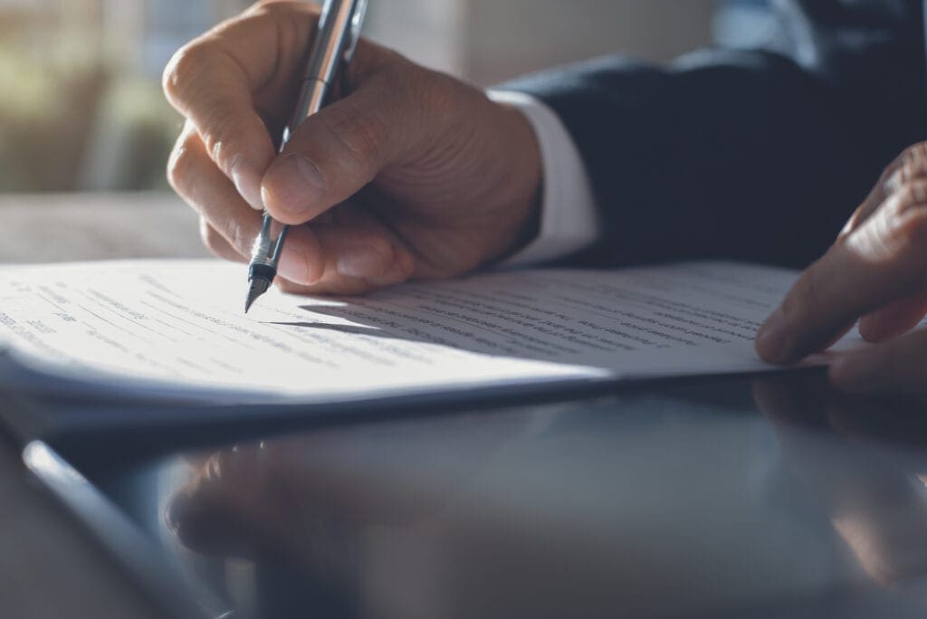 Business man in black suit signing contract document with ldigital tablet on office desk, deal concept, close up